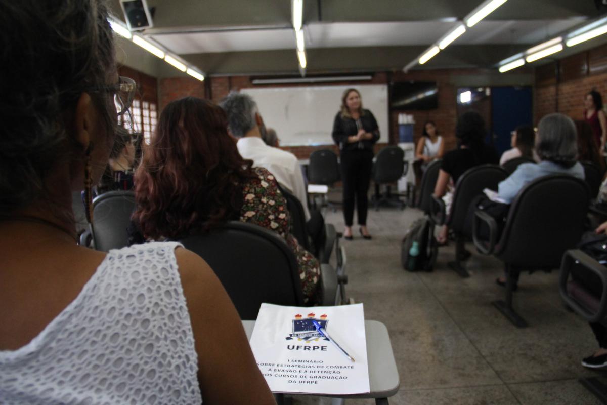 Pasta com nome do evento e pró-reitora no segundo plano 