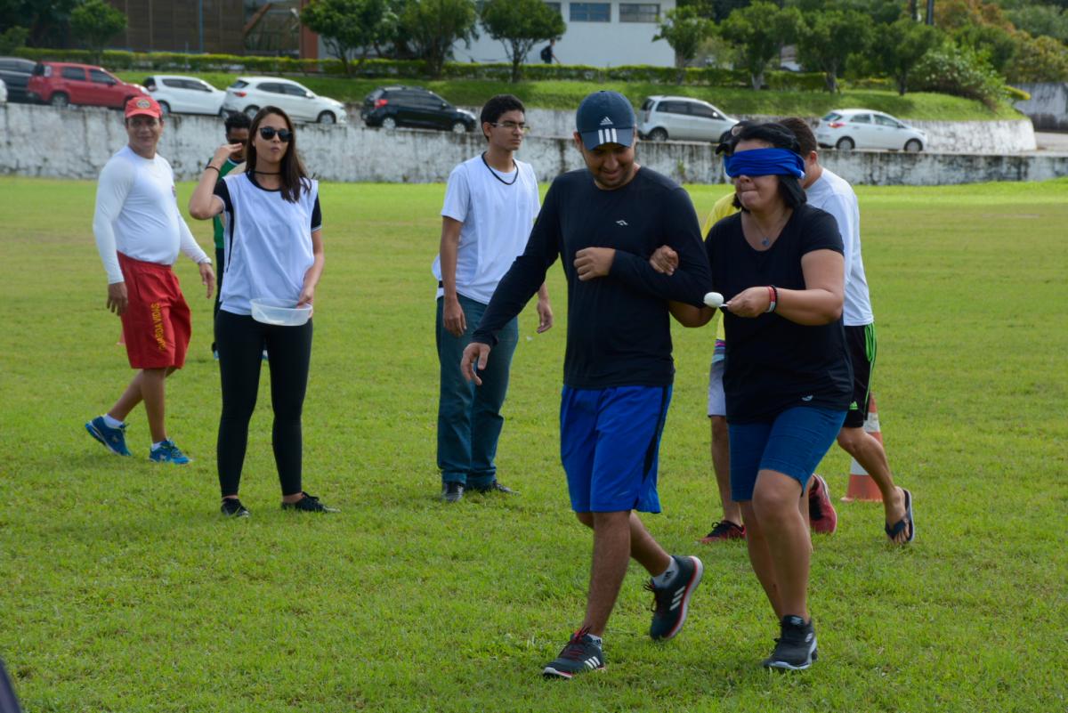 corrida do ovo: estudante mulher vendada segura colher com ovo dentro sendo conduzida por estudante homem